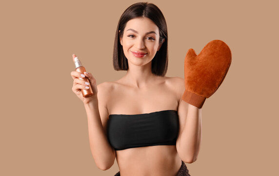 Young woman with massage glove and bottle of self tanner mousse on beige background