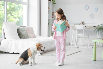 Obraz premium Cute little girl with Beagle dog reading book in bedroom