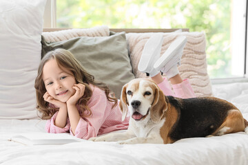 Obraz premium Cute little girl with Beagle dog reading book on bed in bedroom
