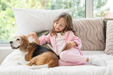 Obraz premium Cute little girl with Beagle dog reading book on bed in bedroom