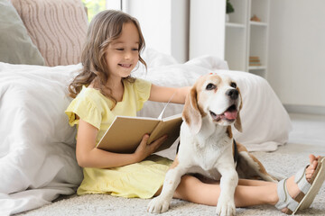 Obraz premium Cute little girl with Beagle dog reading book on floor in bedroom