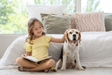 Obraz premium Cute little girl with Beagle dog reading book on floor in bedroom