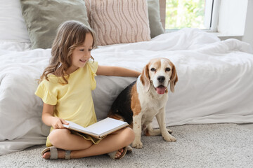 Obraz premium Cute little girl with Beagle dog reading book on floor in bedroom