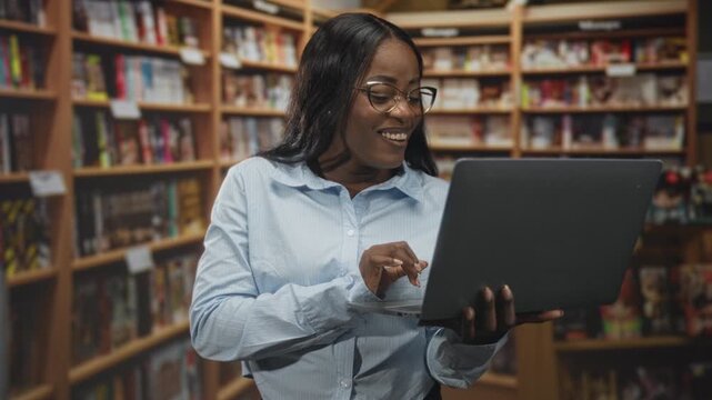 Woman typing on laptop, smiling and holding computer in bookstore building; focused learning happy growth.
