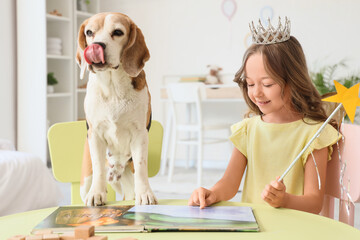 Obraz premium Cute little girl with Beagle dog reading book at table in bedroom