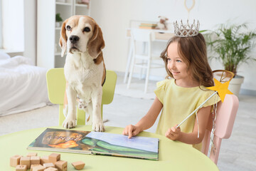 Obraz premium Cute little girl with Beagle dog reading book at table in bedroom