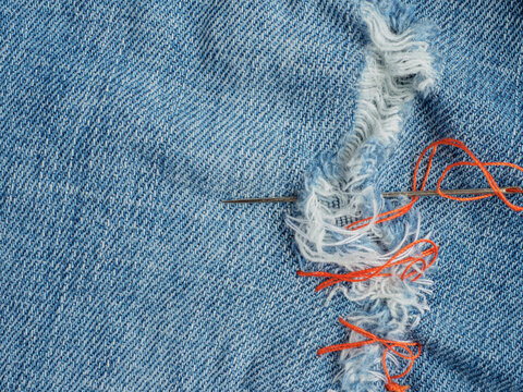 Close up of repairing torn denim fabric with needle and thread