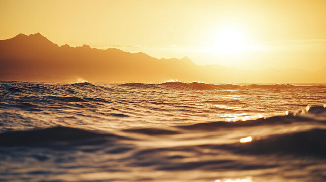 Warm sunset casts golden hues over vast ocean with gentle waves and distant mountain silhouettes creating peaceful and serene natural landscape scene