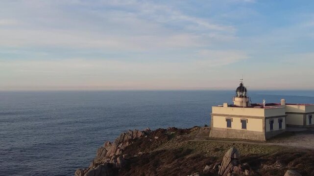 Stunning aerial view showing the historic lighthouse at prior cape in galicia, spain, standing on a rugged cliffside as the calm blue atlantic ocean stretches to the horizon at sunset