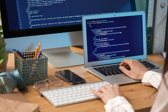 Female programmer's hands working with computer and laptop at table in office, closeup