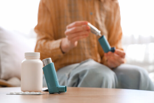 Woman changing asthma aerosol canister, focus on modern inhaler and pills