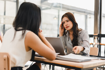 Stressed Asian businesswoman touching her head while pointing at documents during a difficult...