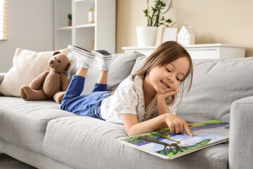 Obraz premium Cute little girl reading story on sofa at home