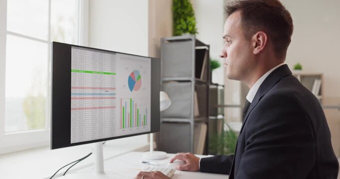 Man analyst working on finance data report. On a computer in an office, an accountant examines spreadsheets, charts, and graphs for audit planning. Clear financial data analysis concept.