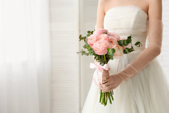 Young woman in wedding dress with bouquet of beautiful ranunculus flowers at home, closeup
