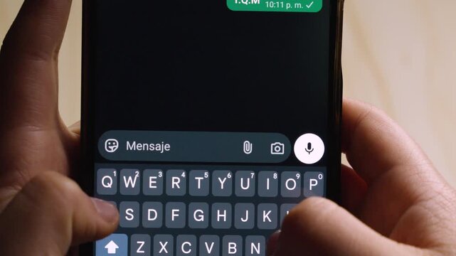Close-up of hands typing the Spanish acronym "T.Q.M" (Te Quiero Mucho) on a smartphone. 