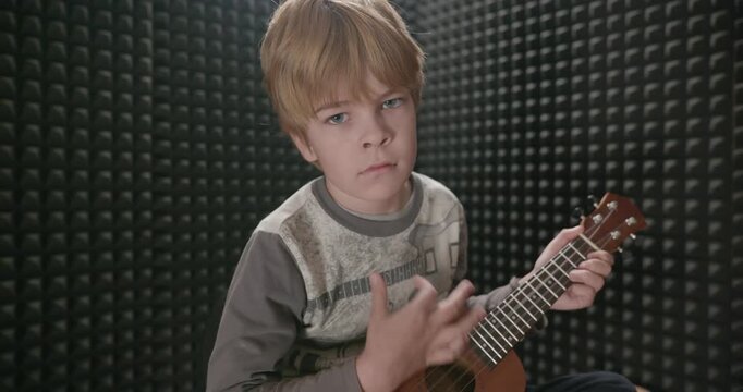 Boy Play Music on Ukulele Instrument in Home Studio. 4K 10-bit