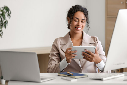 Young African-American QA engineer working with tablet computer at her workspace in office