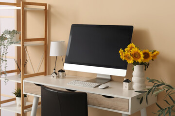 Blank computer monitor and vase and sunflowers on desk in office