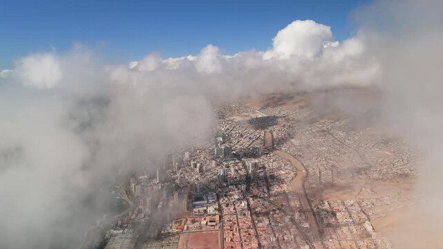A smooth 22-second aerial drone flight from a DJI Mini 4 Pro, flying over thick white coastal fog (camanchaca) to reveal the urban skyline of Antofagasta, Chile. The shot moves from the Pacific Ocean