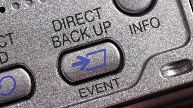 Angled macro close up of direct back up button pressed on metallic silver panel with blue icon