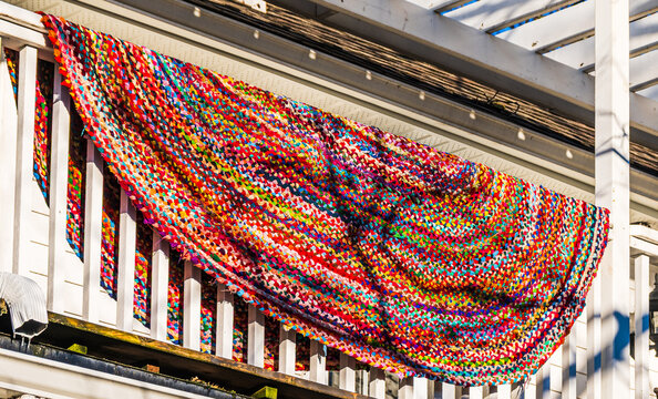 Colourful traditional braided rag rug with hit or miss pattern draped over white balcony railing airing in spring sunshine.