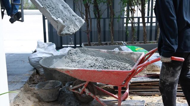 Pouring wet cement concrete from a truck mixer chute into a large mixing tub at a residential construction site. Professional building process and infrastructure development.