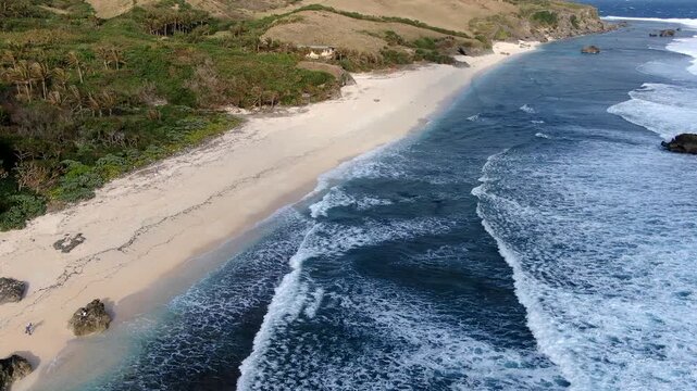 Aerial view of the pristine white sand and rugged coastal landscape of Morong Beach with rolling ocean waves in Sabtang Island, Batanes, Philippines