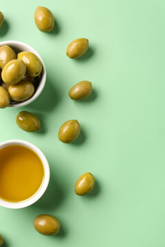 Bowls with ripe olives and oil on green background