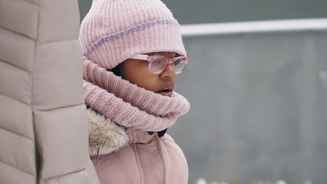 Child in winter attire watches snow fall outside
