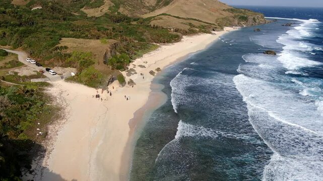 Aerial pullback shot revealing the pristine white sand and rugged coastal landscape of Morong Beach with rolling ocean waves in Sabtang Island, Batanes, Philippines