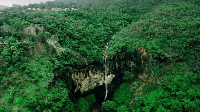Cinematic aerial view of a deep green forest valley with a waterfall or river.