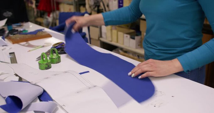 Sewing workshop. Clothing production. Female seamstress folding cut blue fabric pattern draft on table with tailor professional tools.