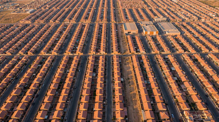 Obraz premium An extensive aerial perspective reveals a large-scale suburban housing development interspersed with commercial or industrial structures under a clear sky.