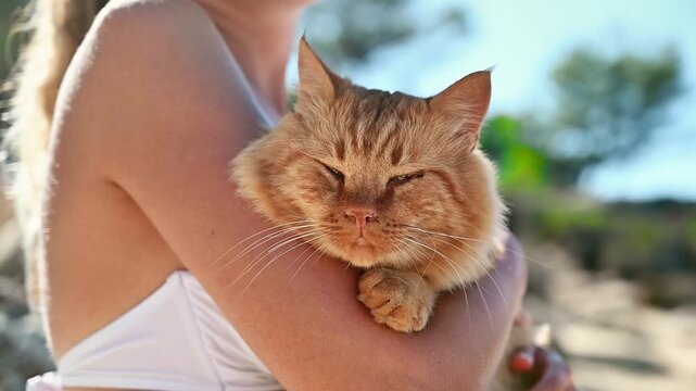 Woman holding affectionate ginger cat outdoors enjoying sunny day.