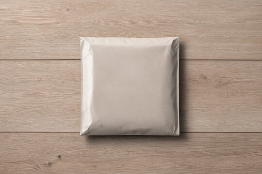 Top view of a blank square mailing envelope or padded poly mailer mockup resting on a light wood surface.