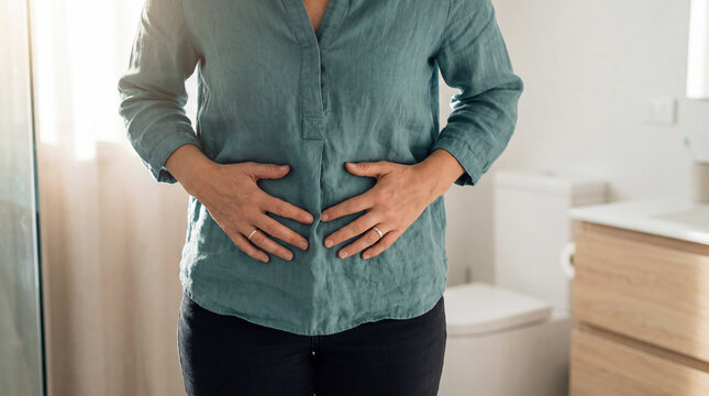 Woman experiencing stomach pain, bloating, or digestive issues, holding her belly in a bathroom setting