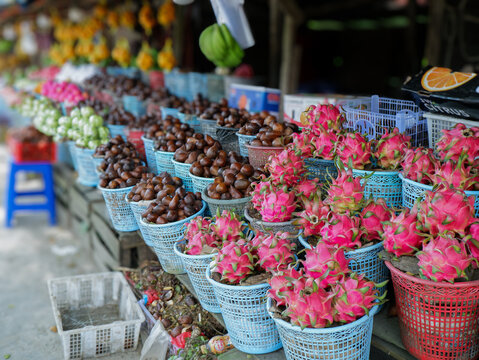 ​Fresh tropical fruits like dragon fruit, salak, and duku arranged in blue baskets at a bustling traditional Asian street market stall