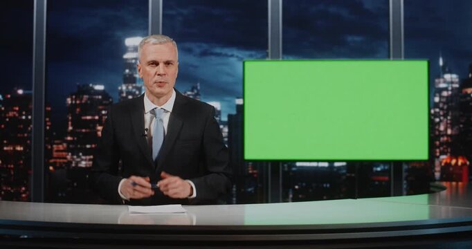 Male Anchor in Suit Sits at Desk With Papers and Pen. Near Man Large Green Chroma Key Screen, Ready For Virtual Background Insertion. Concept of Television Production and News Broadcasting Preparation