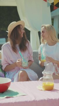 Relaxed friends sharing juice in garden setting, Two pals having laidback outdoor brunch with drinks