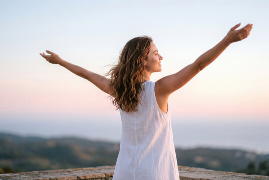 Elegant woman with arms outstretched facing the sunset view