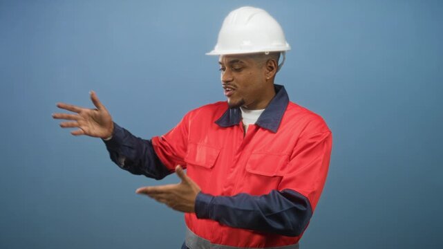 Construction worker man in white hard hat and red work uniform pointing and gesturing hands in studio; instructional safety.