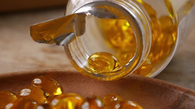 softgel capsules pouring out of opened glass bottle onto wooden plate, supplement herbal extract health concept