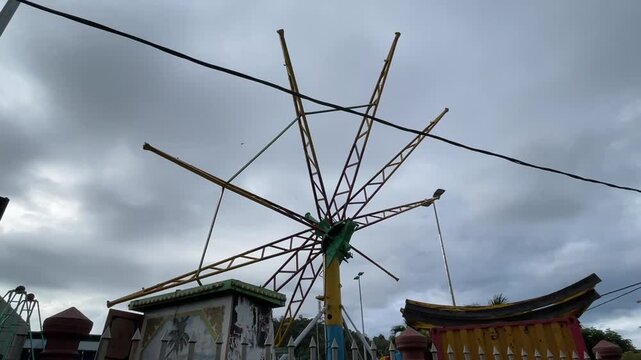 A Paratrooper umbrella ride under installation where the metal bracket rotates slightly with birds flying across a cloudy evening sky.