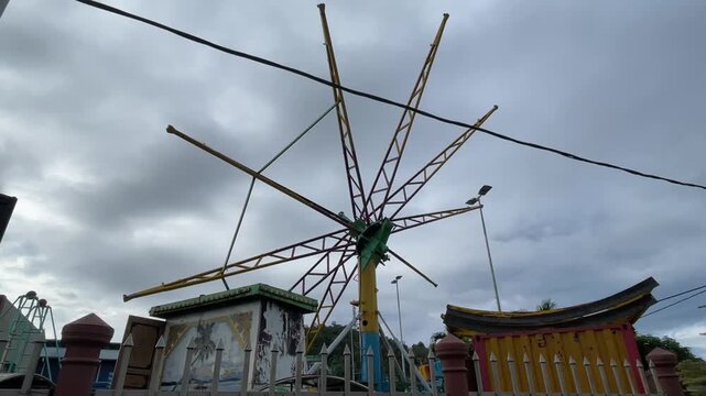 A Paratrooper umbrella ride under installation at a funfair where the metal bracket rotates slowly then stays still against a cloudy evening sky.