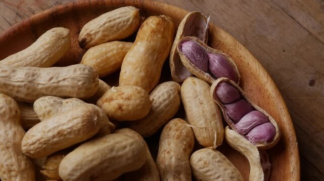 Boiled peanuts in shell with purple violet skin kernels revealed on wooden plate on rustic wood table, healthy traditional Asian snack nutrition closeup