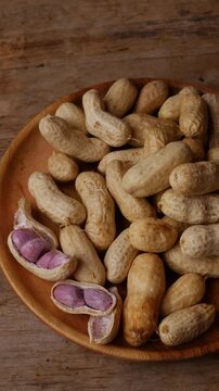 Boiled peanuts in shell with purple violet skin kernels revealed on wooden plate on rustic wood table, healthy traditional Asian snack nutrition closeup