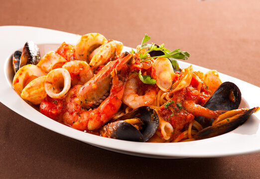 Rich seafood spaghetti with prawns, mussels, squid, and clams in tomato sauce on a white plate.
