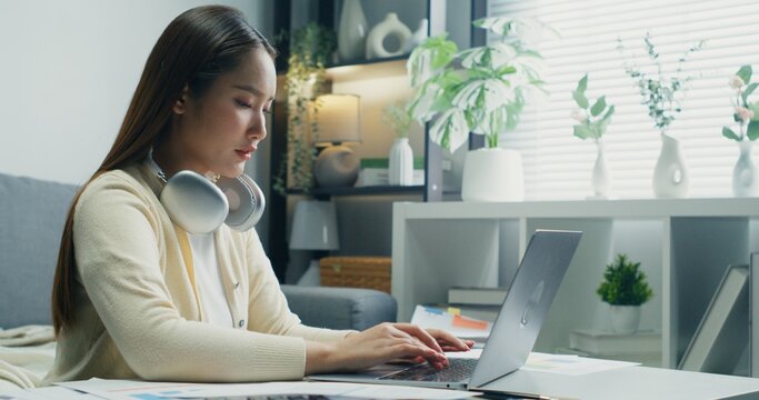 Woman Balancing Corporate Budgets.An Asian woman balances corporate budgets and expense trackers, inspecting financial documents for cost-effective business planning.