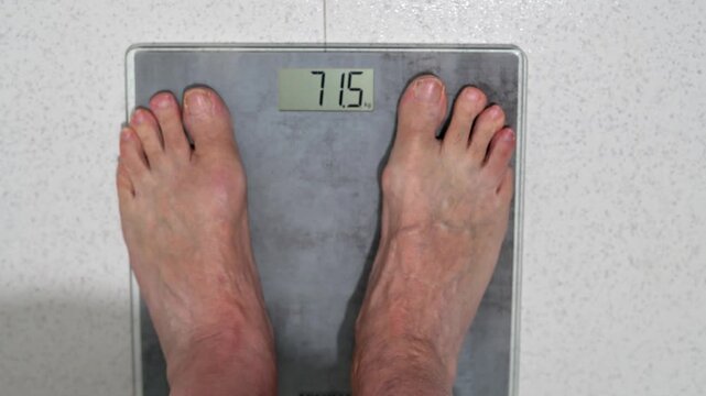 Man Standing On Digital Bathroom Scale Showing Weight Measurement 